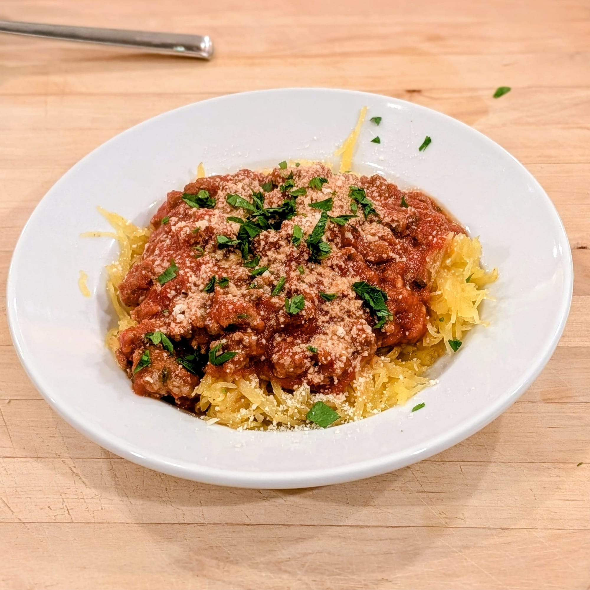 Bonus action shot of a finished plate of Spaghetti Squash with a meat sauce and garnished with parsley and parmesan cheese.  Yum!