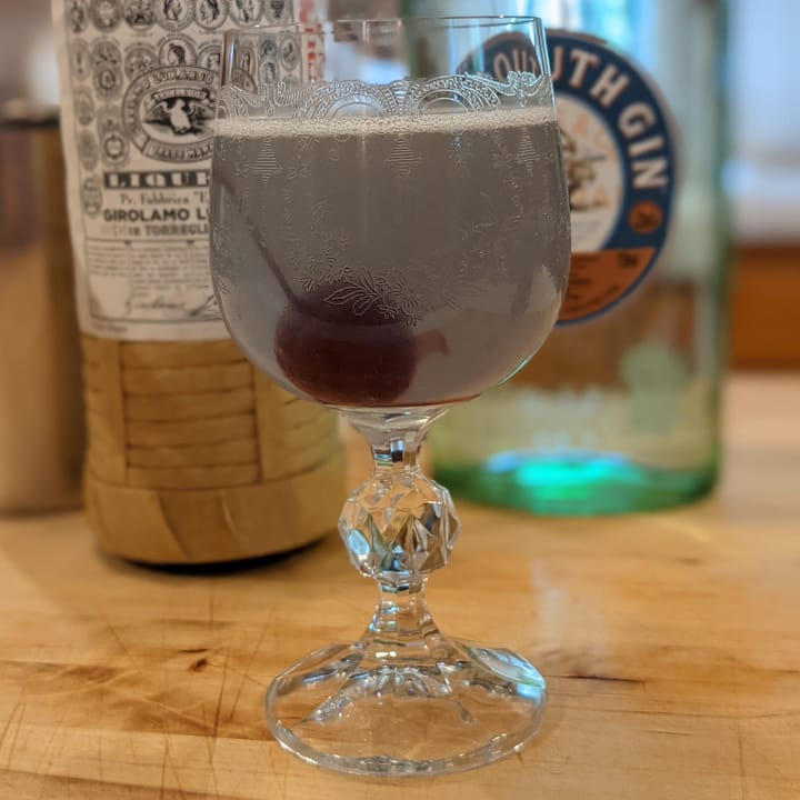 Aviation cocktail in front of liquor bottles.
