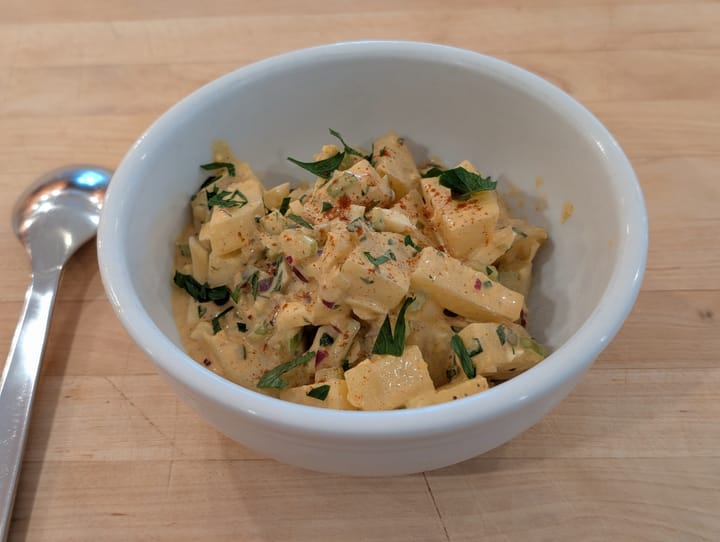 A quite handsome looking bowl of Egg Potato Salad with a spoon ready to dig in.