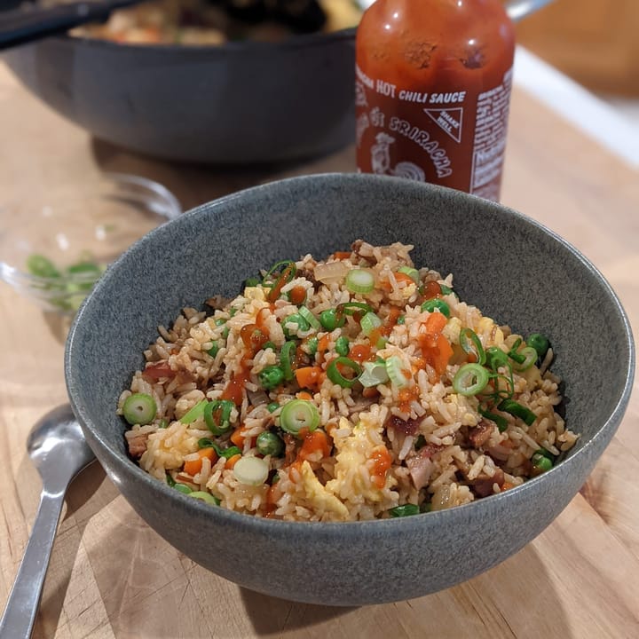 Fried rice in a ceramic bowl with Sriracha hot sauce drizzled over it.