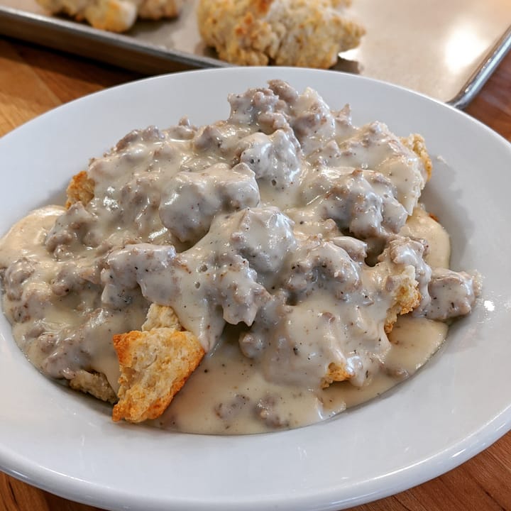 A small portion of heart stopping Sausage Gravy in a bowl over Drop Biscuits.